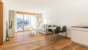 Una habitación de hotel moderna con suelo de madera, un área de comedor con mesa y sillas, un sofá y una cocina.
