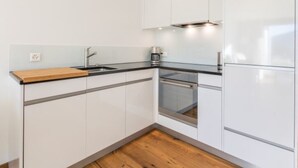 Una cocina moderna con armarios blancos, encimera de madera, pileta de acero inoxidable y horno empotrado.