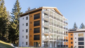 Un edificio moderno de varios pisos con fachada de vidrio y madera, rodeado de árboles.