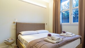 A hotel room with a bed, a bedside table with a magazine, and a window with curtains. - Flower Residence - Appartamento Begonia (Lissone)