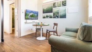 Uma sala de estar com sofá, mesa de jantar com cadeiras, televisão de tela plana e parede decorada com quadros.
