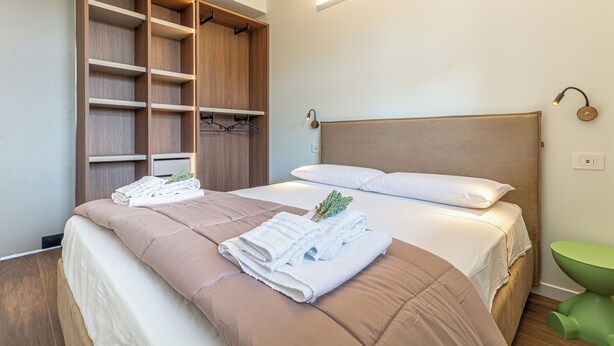 Quarto com uma cama, um guarda-roupa de madeira e uma cadeira verde.
