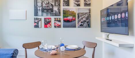 A dining area with a round table, two chairs, a flat-screen TV, and wall-mounted artwork.