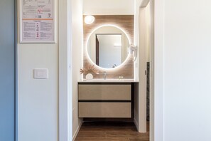 Ein modernes Badezimmer mit einem runden Spiegel, einem Fön und einem Waschbecken.