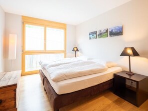 Un dormitorio con una cama, dos lámparas de noche, una mesita de noche, una ventana y tres cuadros colgados en la pared.