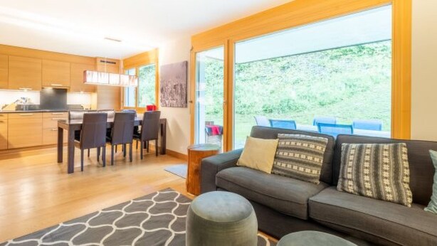 Ein modernes Wohnzimmer mit einer Couch, Poufs und einem Essbereich mit Stühlen und einem Tisch.