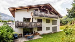 Ein zweistöckiges Gebäude mit Balkon, Terrasse, Tisch und Stühlen sowie einem gepflegten Rasen.