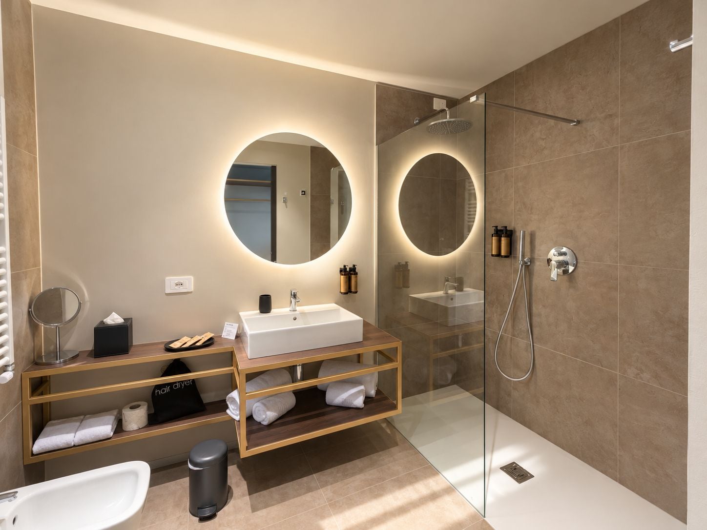 Ein modernes Badezimmer mit einer gläsernen Duschkabine, einem runden Spiegel, einem weißen Waschbecken und einem Waschtisch mit Regalen.