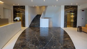 A modern lobby with a marble floor, a central staircase, and two elevators.