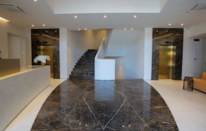 A modern lobby with a marble floor, a central staircase, and two elevators. - Elitis House Suite & Spa (Nova Milanese)
