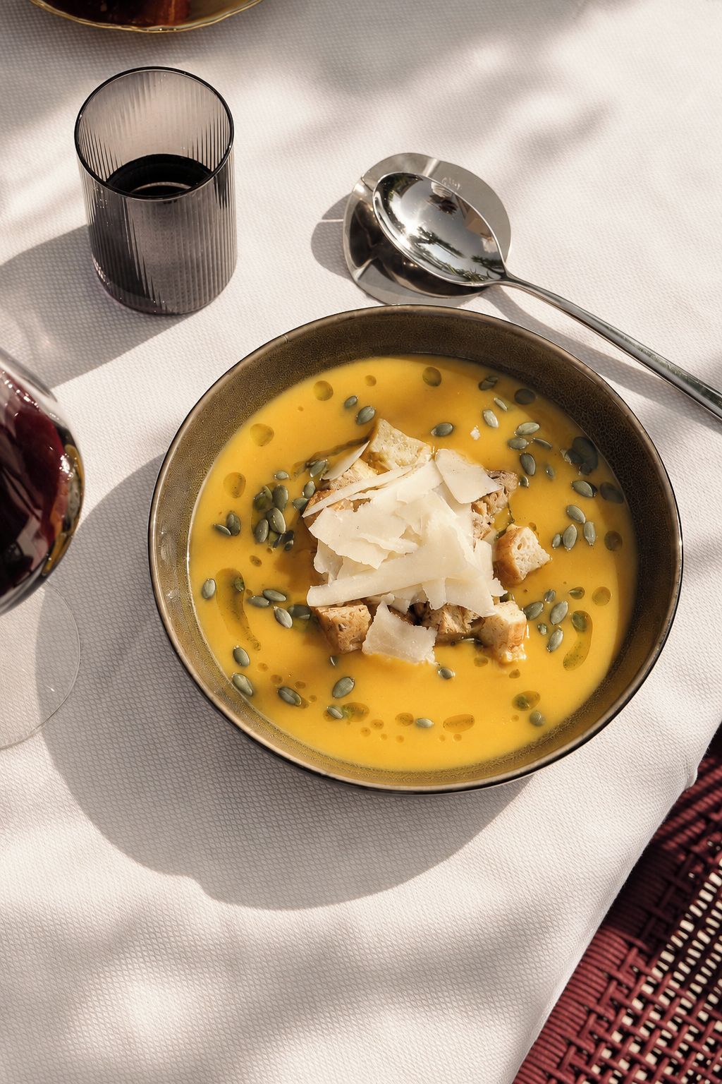Un bol de soupe garni de graines de courge et de croûtons, posé sur une nappe.