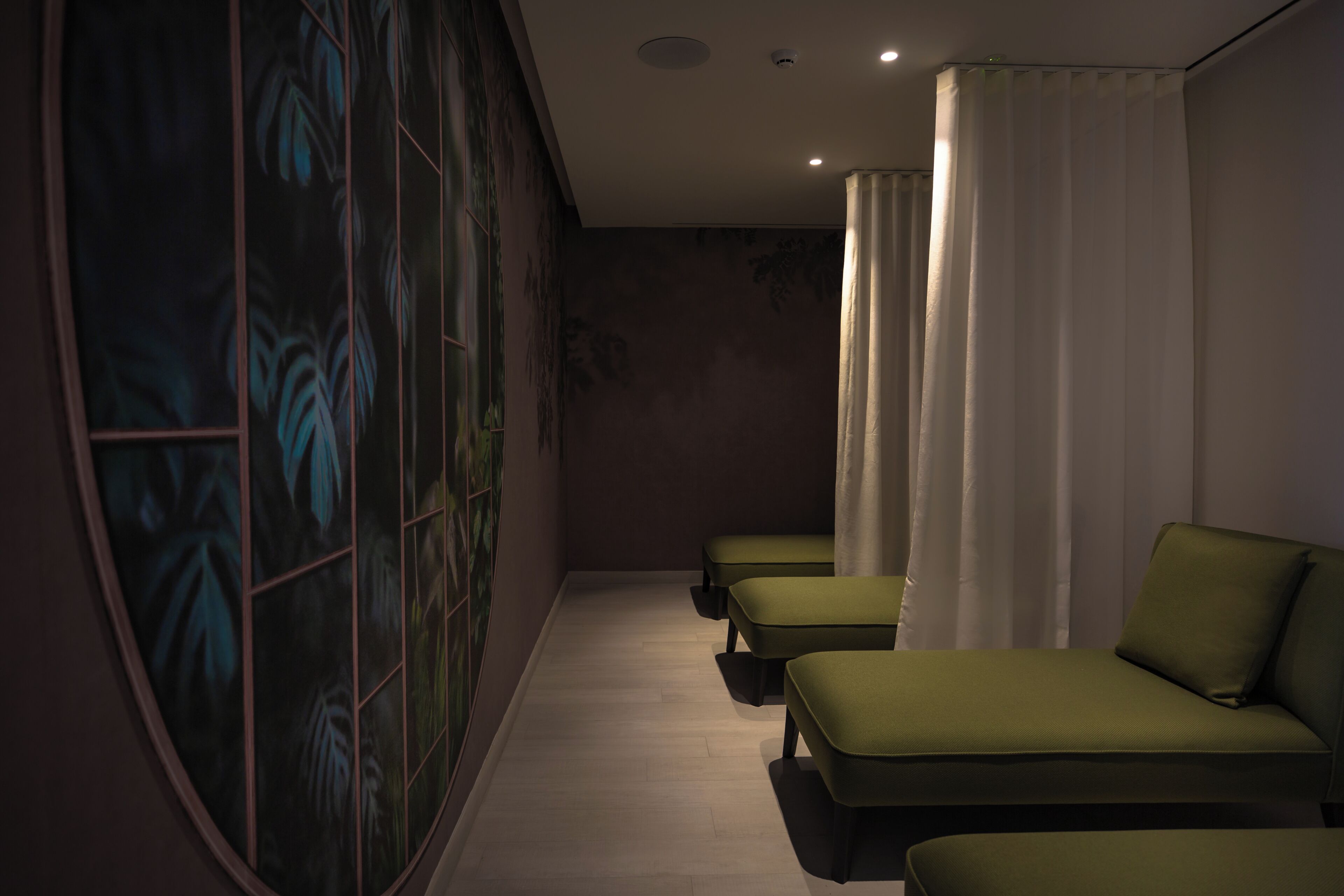 Ein Wellnessraum mit Massageliege, Massagesessel und Wand mit Blättermotiv.