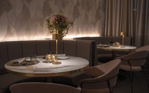 A restaurant with round tables, cushioned seating, and a vase with flowers. - Elitis House Suite & Spa (Nova Milanese)