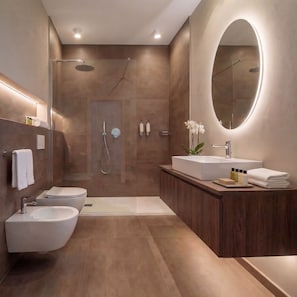 Ein modernes Badezimmer mit barrierefreier Dusche, zwei Waschbecken, einem großen Spiegel und einem Waschtisch mit Pflegeprodukten.
