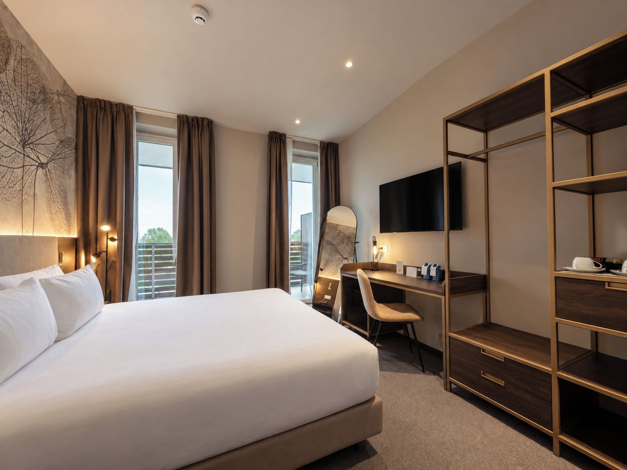 A hotel room with a large bed, a desk, a chair, a wardrobe, a flat-screen TV, and a window with curtains.