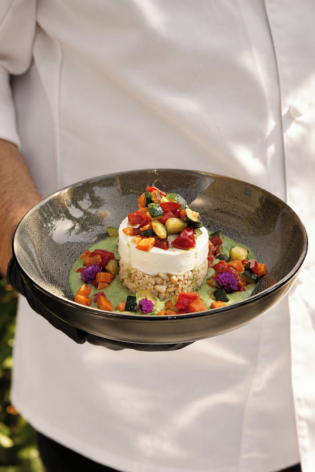 A person holding a plate with a layered dish, possibly a dessert, with a creamy top layer and a base of grains or rice.
