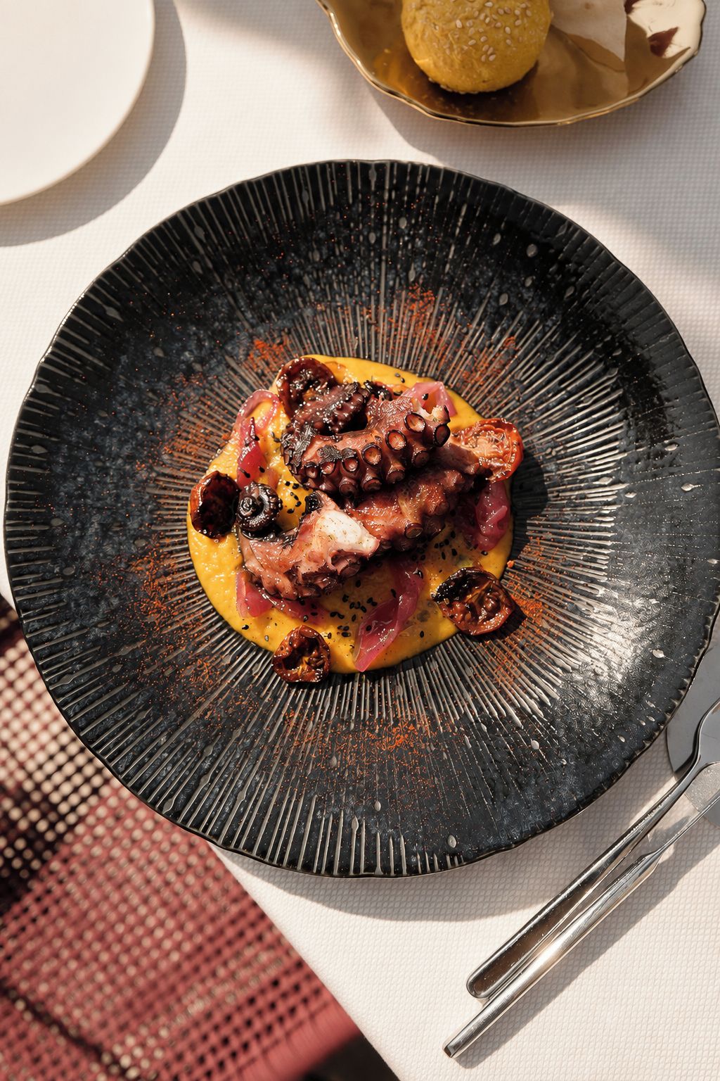 A black plate with a food dish, a spoon, and a napkin on a table.