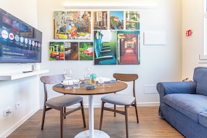 Ein modernes Wohnzimmer mit einem Flachbildfernseher, einem runden Esstisch mit zwei Stühlen, einer Couch und einer Wand mit Reisekunstwerken.