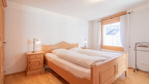 A bedroom with a wooden bed, two bedside tables with lamps, a window with curtains, and a wooden floor. - Capolgarten 3.7 by Interhome (Flims)