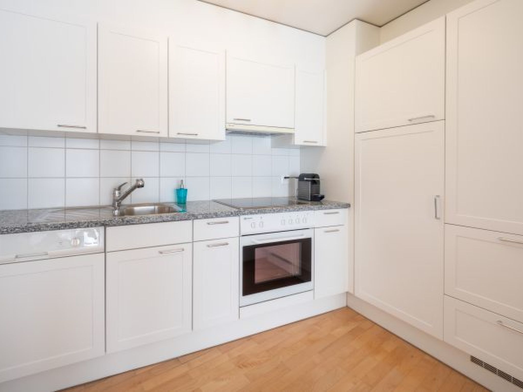 A kitchen with white cabinets, a granite countertop, a sink, a coffee maker, and an oven.