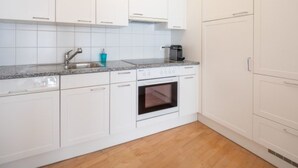 A kitchen with white cabinets, a granite countertop, a sink, a coffee maker, and an oven. - Capolgarten 3.7 by Interhome (Flims)