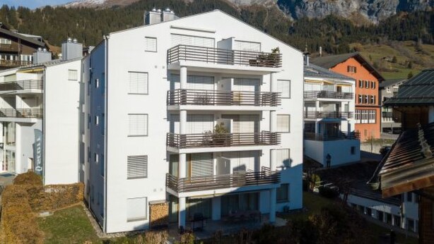 A multi-story building with balconies, surrounded by mountains and other residential buildings. - Capolgarten 3.7 by Interhome (Flims)