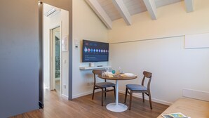A modern room with a dining table, two chairs, a flat-screen TV mounted on the wall, and a wooden floor. - Flower Residence - Appartamento Iris (Lissone)