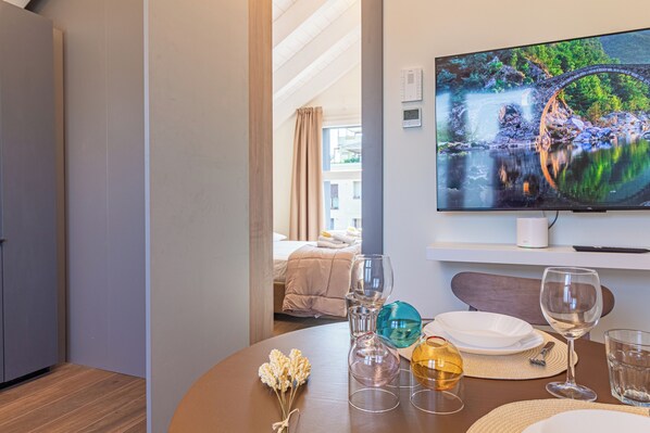 Ein Hotelzimmer mit einem Bett, einem an der Wand befestigten Fernseher und einem Esstisch mit Gläsern und Tellern.