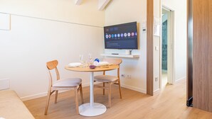A modern room with a round table, two chairs, a flat-screen TV mounted on the wall, and a wooden door. - Flower Residence - Appartamento Narciso (Lissone)