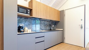 A modern kitchen with a microwave, wooden cabinets, a marble backsplash, and a door to the right. - Flower Residence - Appartamento Narciso (Lissone)