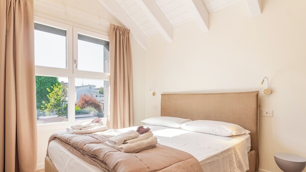 A neatly made bed with a headboard, a bedside table, and a window with curtains. - Flower Residence - Appartamento Narciso (Lissone)