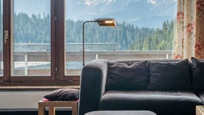 Een kamer met een groot raam, een bank, een kleine tafel en een lamp.