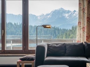 Een kamer met een groot raam, een bank, een kleine tafel en een lamp.