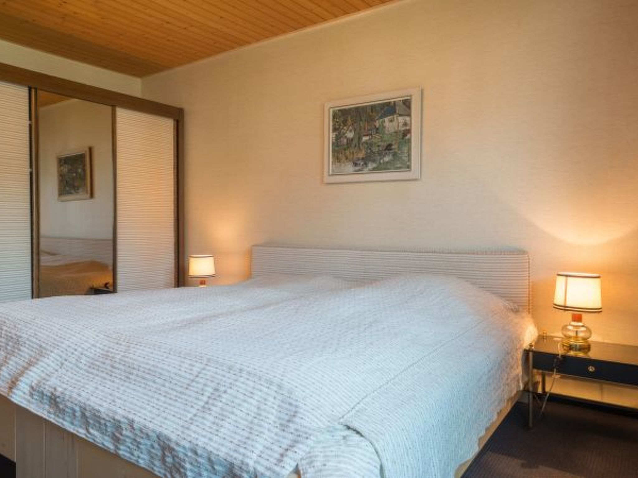 Un dormitori amb un llit, dues làmpades de nit, un quadre a la paret i un mirall.