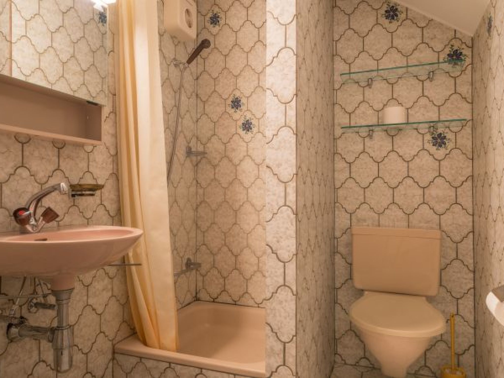 Une salle de bain équipée d’un lavabo, d’une douche, de toilettes et d’une étagère où sont rangés les articles de toilette.
