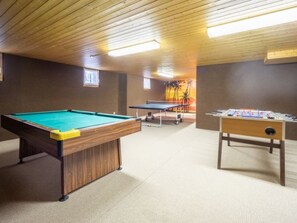 Une table de billard, une table de baby-foot et une table de ping-pong se trouvent dans une pièce dont le plafond et les murs sont en bois.