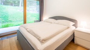 A bedroom with a bed, a nightstand, a lamp, and a window with a view of a grassy area. - Residenz Cuolm Liung 52 by Interhome (Laax)