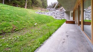 A modern building with a concrete exterior, a stone wall, and a grassy slope. - Residenz Cuolm Liung 52 by Interhome (Laax)