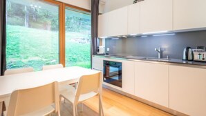A modern kitchen with white cabinets, a built-in oven, and a large window offering a view of a grassy area. - Residenz Cuolm Liung 52 by Interhome (Laax)