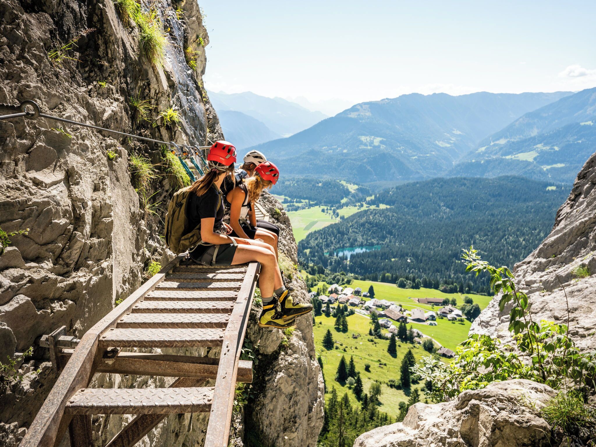 Un escalier en bois menant au sommet d’une montagne, où l’on voit des randonneurs portant des casques et des sacs à dos.