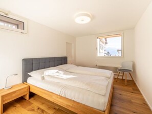 Ein Schlafzimmer mit Bett, Nachttisch, Stuhl, Fenster mit Aussicht und Heizkörper.