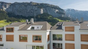 Un edificio residencial con varias ventanas, techo plano y montañas al fondo.