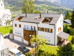 Ein modernes, zweistöckiges Haus mit Garage, Balkon und Blick auf eine gebirgige Landschaft.