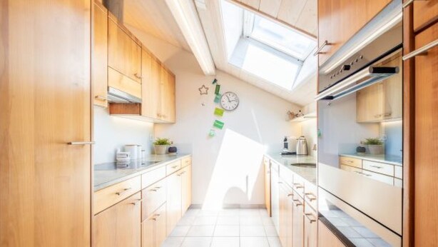 A narrow kitchen with wooden cabinets, a tiled floor, a skylight, and a clock on the wall. - Casa Alva - FLIMS by Interhome (Flims)