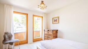 A bedroom with a bed, a chair, a wooden dresser, and two windows with curtains. - Casa Alva - FLIMS by Interhome (Flims)