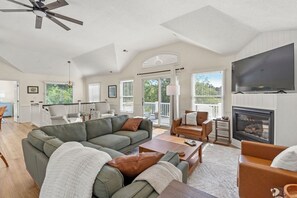 A spacious living room with a large sectional sofa, a fireplace, a television, and a balcony with sliding doors.