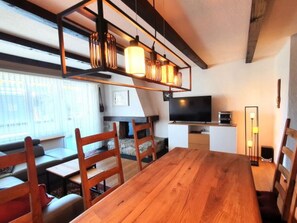 A modern living room with a wooden dining table, chairs, a TV, and a sofa. - Via Sulten 12 by Interhome (Flims)