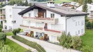 A multi-story building with balconies, a covered outdoor seating area, and a view of a green landscape with mountains in the background. - Via Sulten 12 by Interhome (Flims)