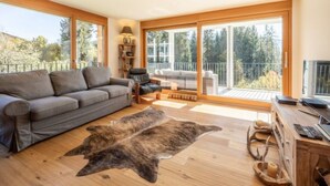 Un salón moderno con un sofá gris, una mesa de centro de madera y un ventanal con vistas a árboles.