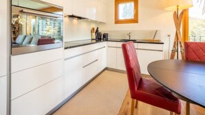 Una cocina moderna con armarios blancos, una mesa de comedor con una silla roja y una ventana con vista a un balcón.